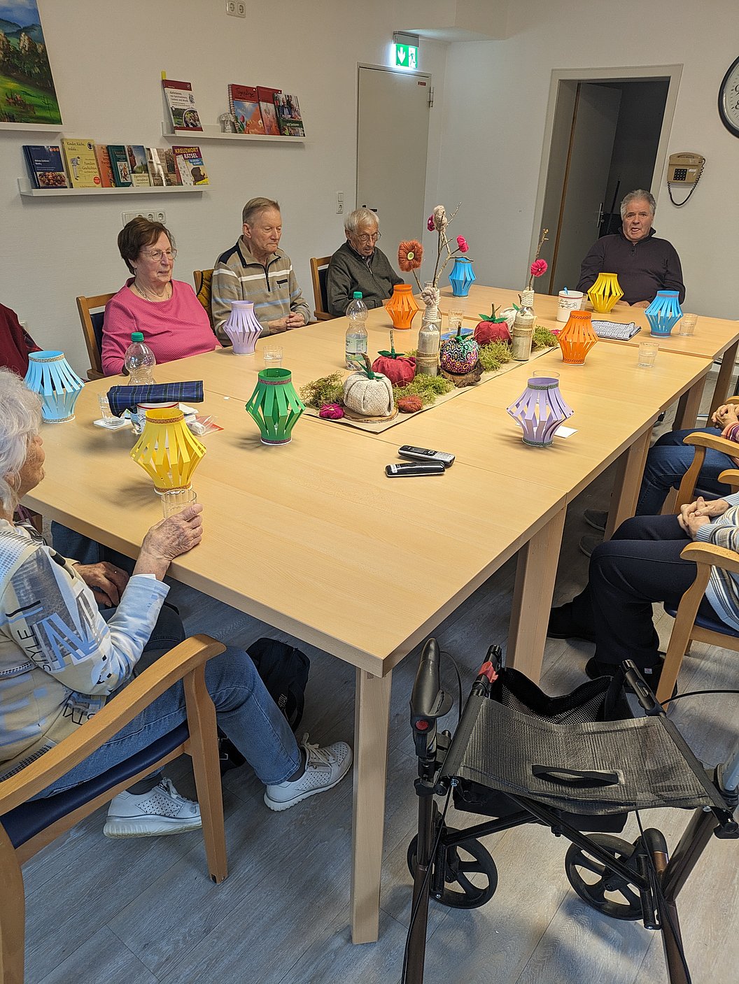 Mehrere ältere Menschen sitzen an einem rechteckigen Holztisch mit bunten Papierlaternen und Bastelmaterialien