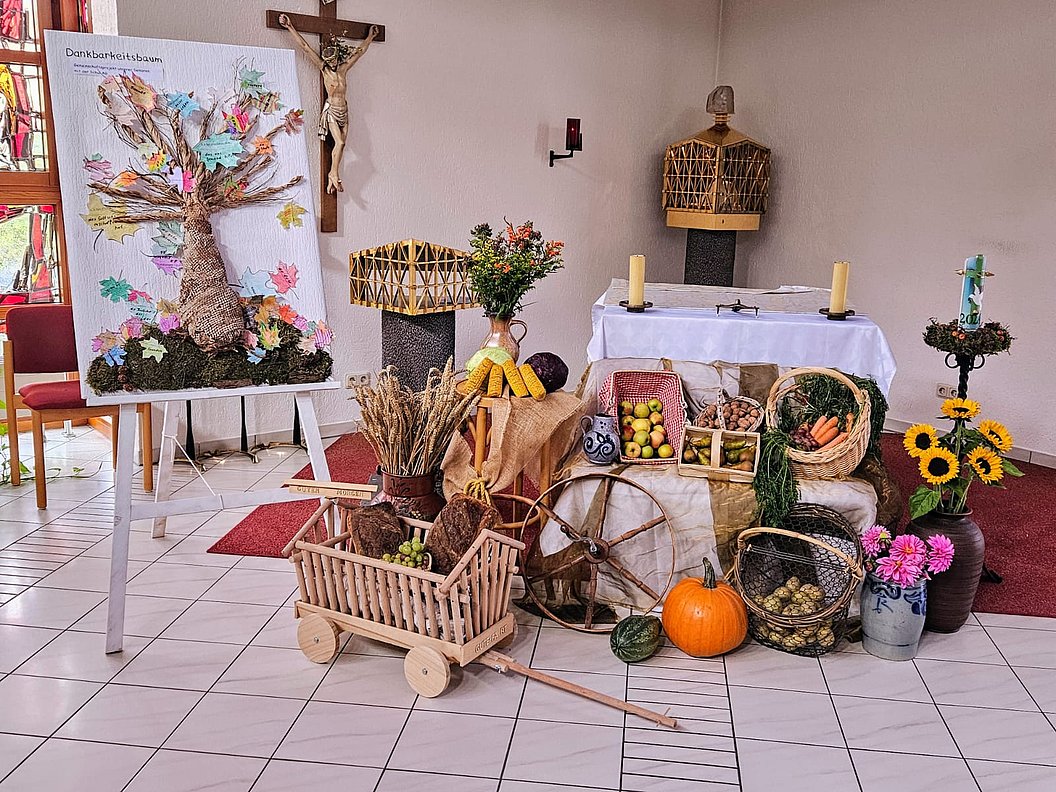 Herbstliche Erntedank-Dekoration mit Baum aus Papierblättern, Kürbissen, Getreidebündeln, Obst und Blumen vor einem Altar in einem Kirchenraum